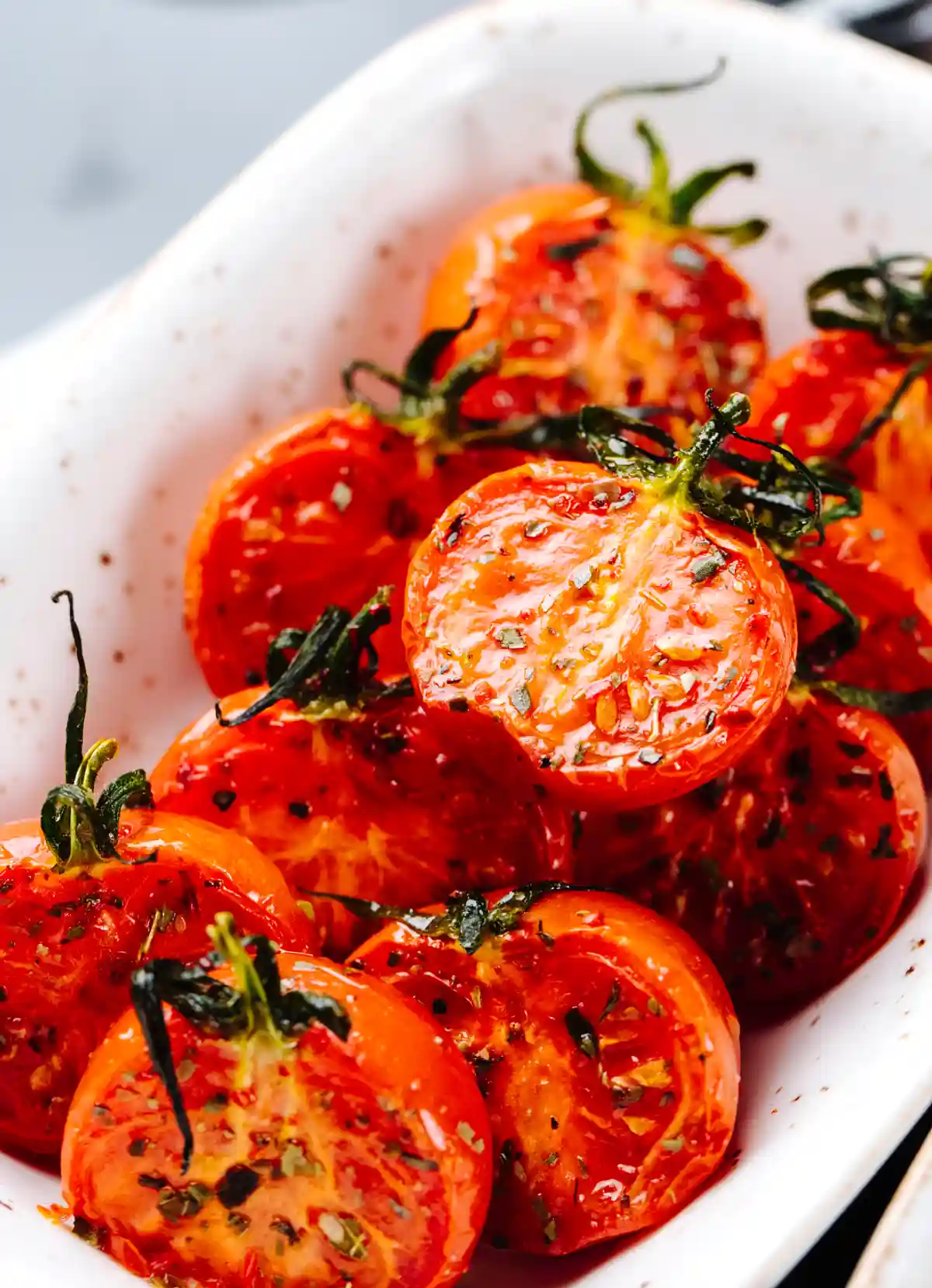 Печени чери домати със зехтин, подправки и пресни билки, сервирани в бяла керамична чиния